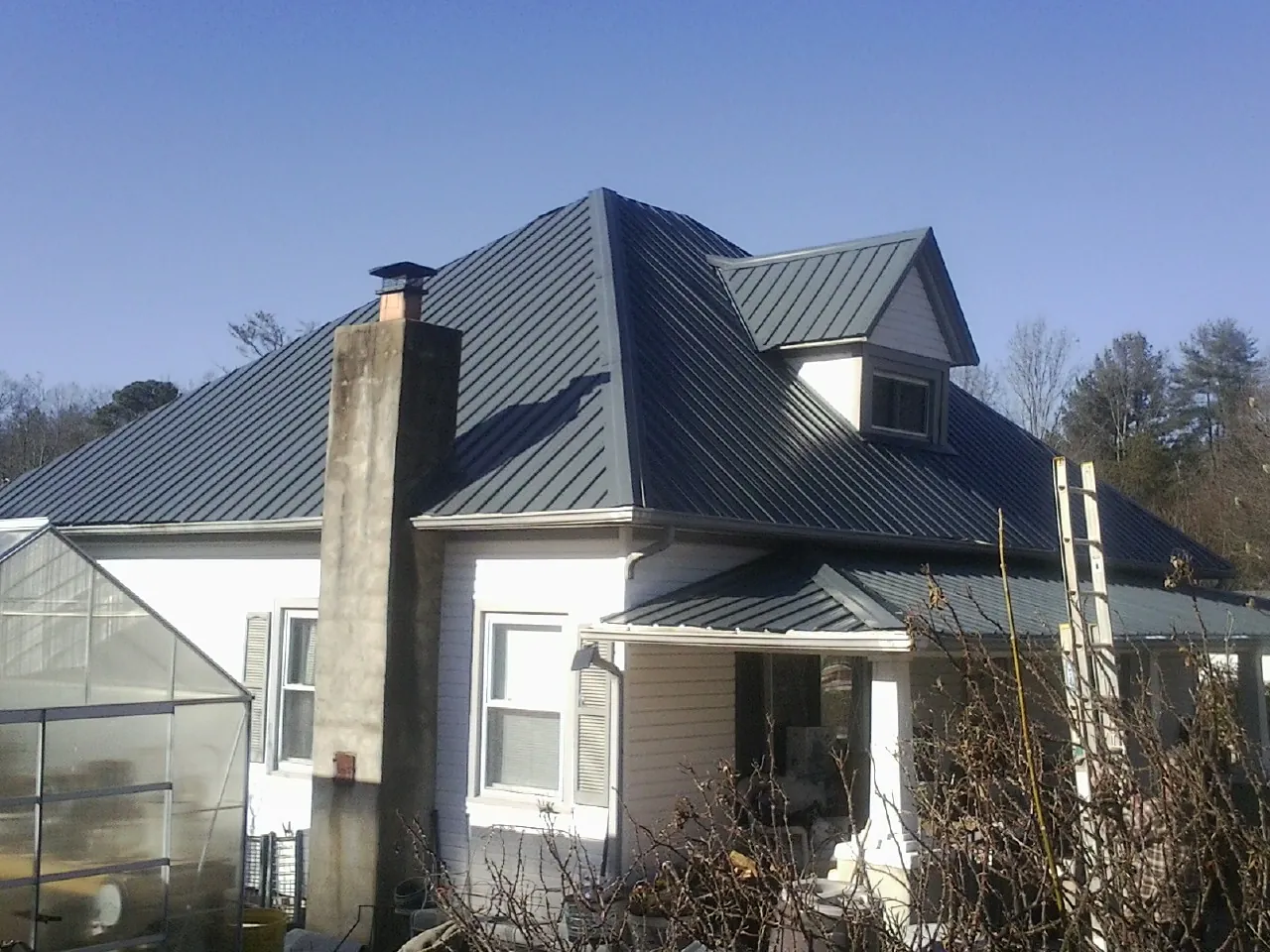 Dark blue standing seam metal roof on a white farmhouse with dormer — Slate & Tile Roof Repair by Roofing Brothers in Wesley Chapel