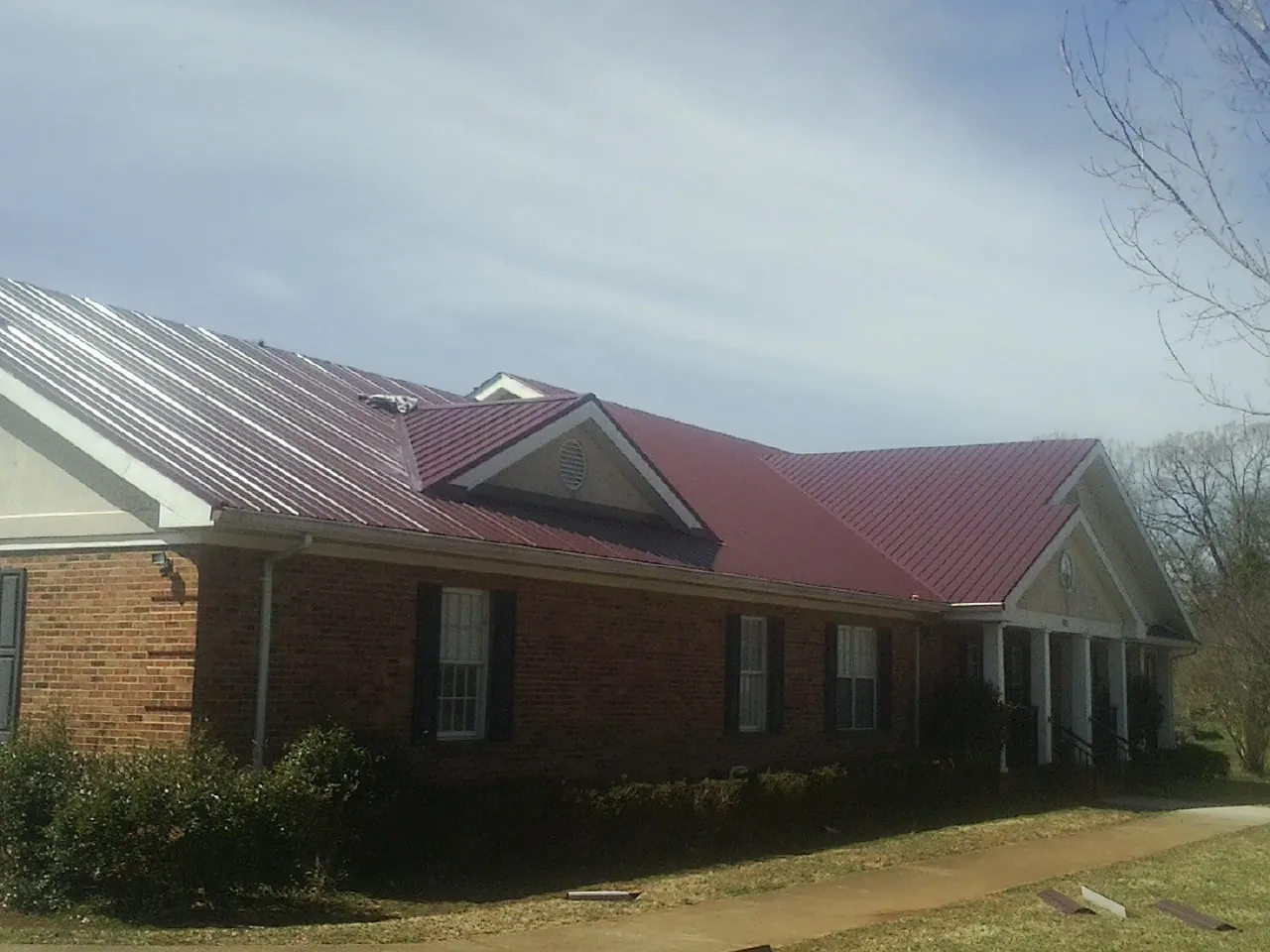 Red metal roof with gabled entries on a long brick building, from a Hail Damage Roof Repair job in Wesley Chapel