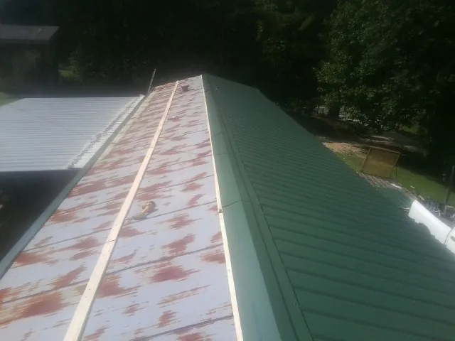 Old rusted panels beside newly installed green metal roofing — Wind Damage Roof Repair by Roofing Brothers in Wesley Chapel