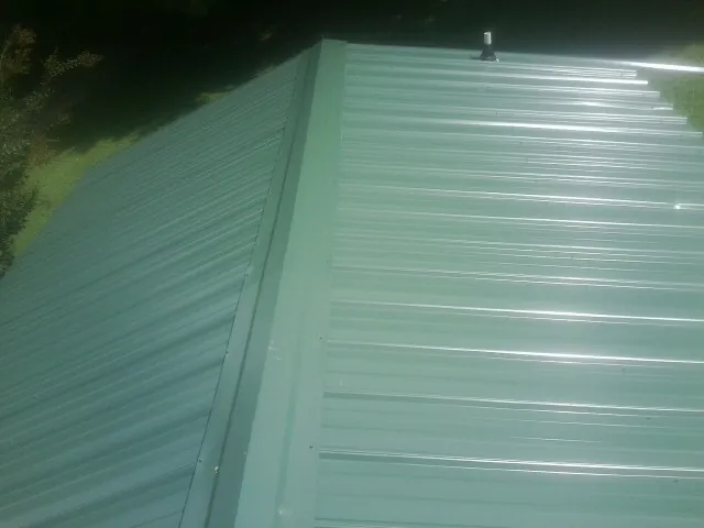 New green metal panels meeting at the ridge of a roof — Flat Roof Repair work by our crew in Wesley Chapel